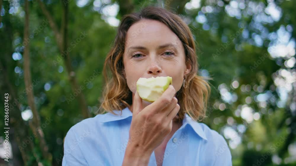 Happy woman eating fruit at park portrait. Lady enjoying apple looking camera Happy woman eating fruit at park portrait. Lady enjoying apple looking camera