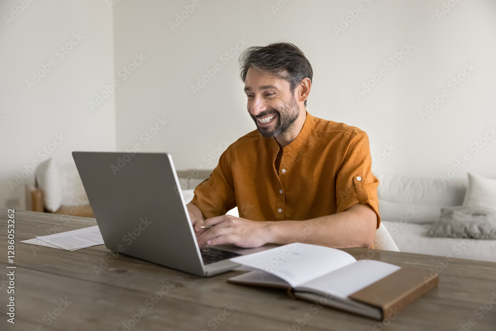 Happy middle-aged man sitting at table using laptop, smiling, reading pleasant news in notice or email, leading online chat, exchanging messages, working, spend time on internet during day-off at home Happy middle-aged man sitting at table using laptop, smiling, reading pleasant news in notice or email, leading online chat, exchanging messages, working, spend time on internet during day-off at home