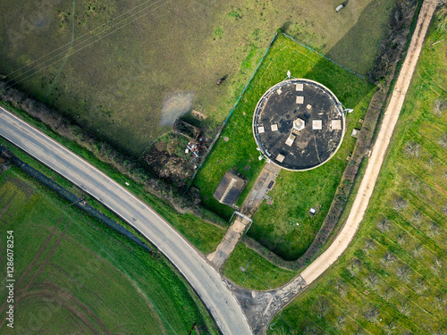 Aerial top down view of a concrete water tower seen in early evening sunlight. Various communications and 5G antennas are on its roof. Seen near a horse paddock in the UK. photo