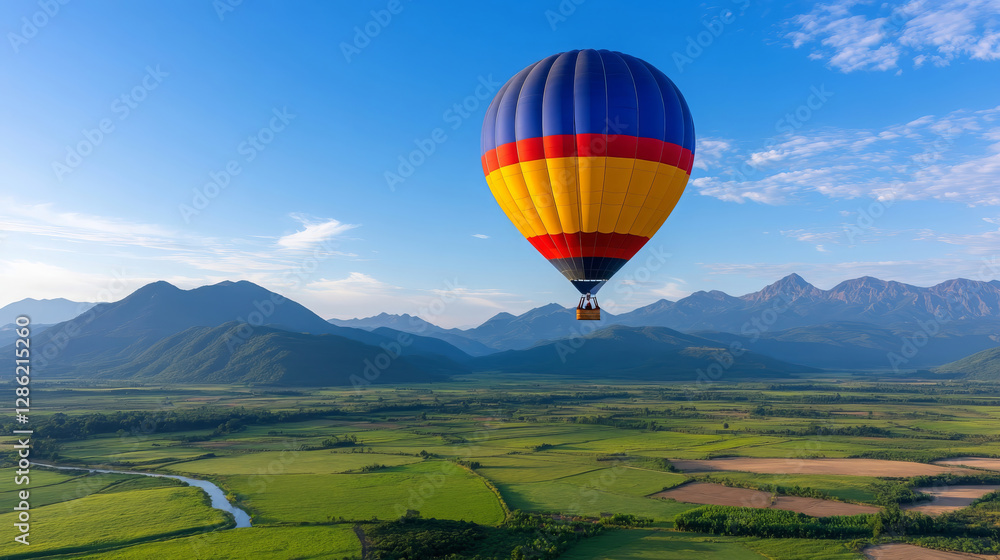 Obraz premium colorful hot air balloon soaring high above lush green fields and mountains, creating breathtaking view of nature beauty. vibrant colors contrast beautifully with blue sky
