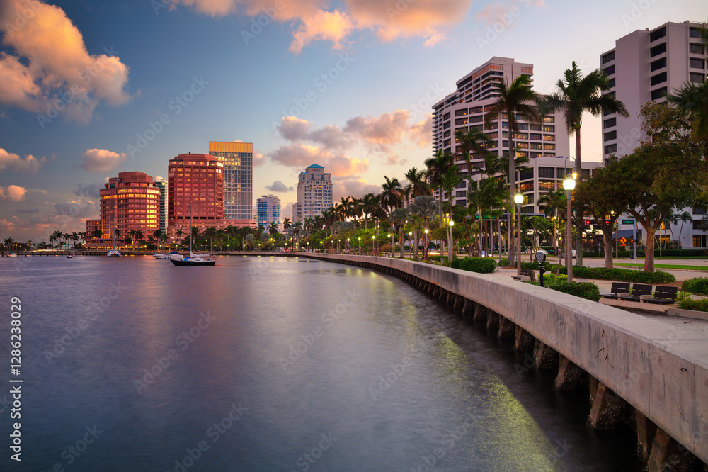 West Palm Beach, Florida, USA. Skyline of West Palm Beach, Florida, at dusk. Tall buildings with reflective glass facades line the waterfront, casting colorful reflections on the water.