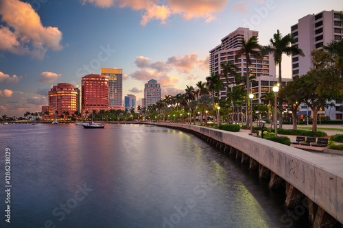 Obraz na płótnie West Palm Beach, Florida, USA. Skyline of West Palm Beach, Florida, at dusk. Tall buildings with reflective glass facades line the waterfront, casting colorful reflections on the water. w salonie