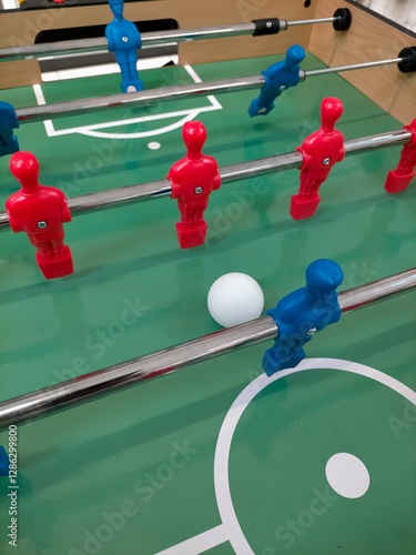 table football in the foreground with players from one team in blue and the other in red with a white ball