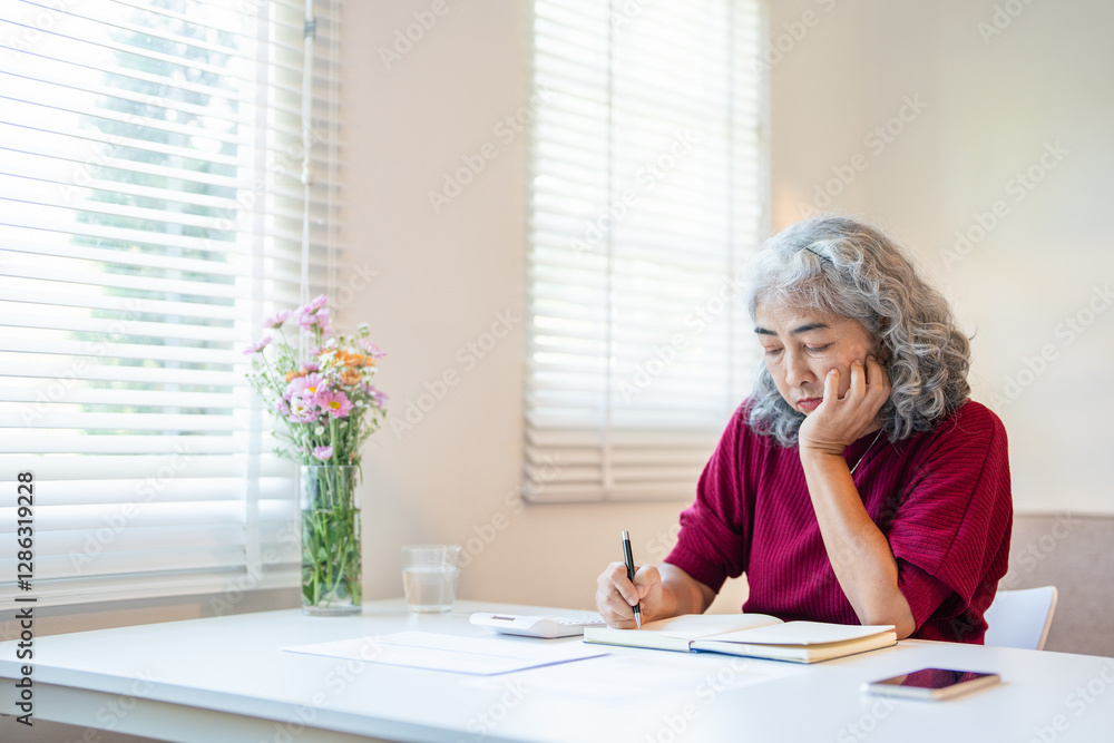 Attractive serious retired female with calculator on table, making notes while managing family budget, writing down numbers, calculating expenses Attractive serious retired female with calculator on table, making notes while managing family budget, writing down numbers, calculating expenses