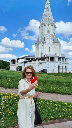 a girl takes a selfie in the park on a sunny summer day against the backdrop of a temple and blooming dandelions, blue sky