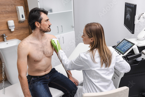 Wallpaper Mural Adult man with shoulder pain getting sonography exam sitting on medical couch near specialist and ultrasound machine at clinic. Comprehensive shoulder US examination Torontodigital.ca