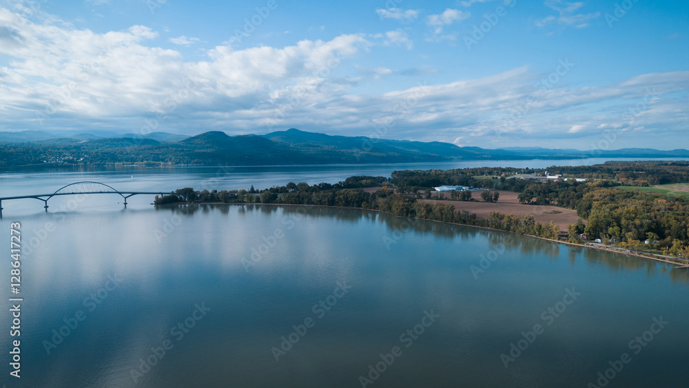 Naklejka premium Aerial view of a bridge spanning a wide river, connecting two lush green landscapes.