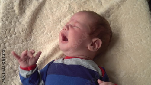 A newborn boy dressed in a striped bodysuit cries due to abdominal pain
