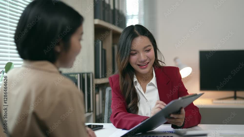 Professional businesswomen reviewing project strategy, leaning over documents, discussing workplace goals in contemporary glass walled corporate meeting room Professional businesswomen reviewing project strategy, leaning over documents, discussing workplace goals in contemporary glass walled corporate meeting room