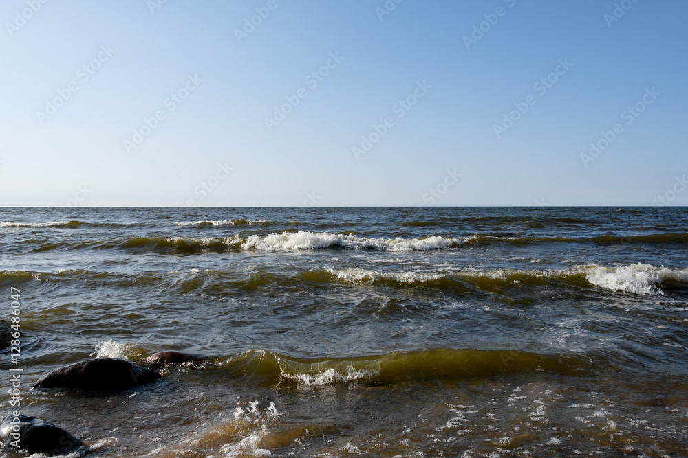 Small foaming sea waves roll in frontally. Blue sky on a sunny summer evening. Light breeze on the seascape Small foaming sea waves roll in frontally. Blue sky on a sunny summer evening. Light breeze on the seascape