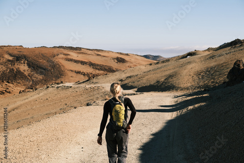 Wallpaper Mural A lone hiker with a backpack walks a scenic mountain trail. The vast, arid landscape and clear blue sky offer a sense of adventure and freedom.Volcano Teide area.Tenerife.Canary Island.Spain Torontodigital.ca