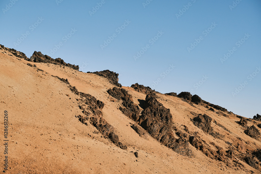 Dramatic landscape photo of a sandy hillside with dark volcanic rocks under a clear blue sky. Perfect for travel, nature, or geological themed projects. Dramatic landscape photo of a sandy hillside with dark volcanic rocks under a clear blue sky. Perfect for travel, nature, or geological themed projects.