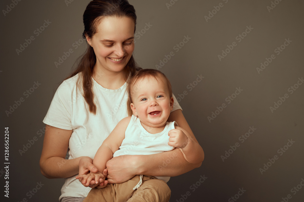 A joyful mother sits with her smiling baby in a calm indoor environment. The baby expresses happiness with an adorable grin while comfortably resting in her arms A joyful mother sits with her smiling baby in a calm indoor environment. The baby expresses happiness with an adorable grin while comfortably resting in her arms