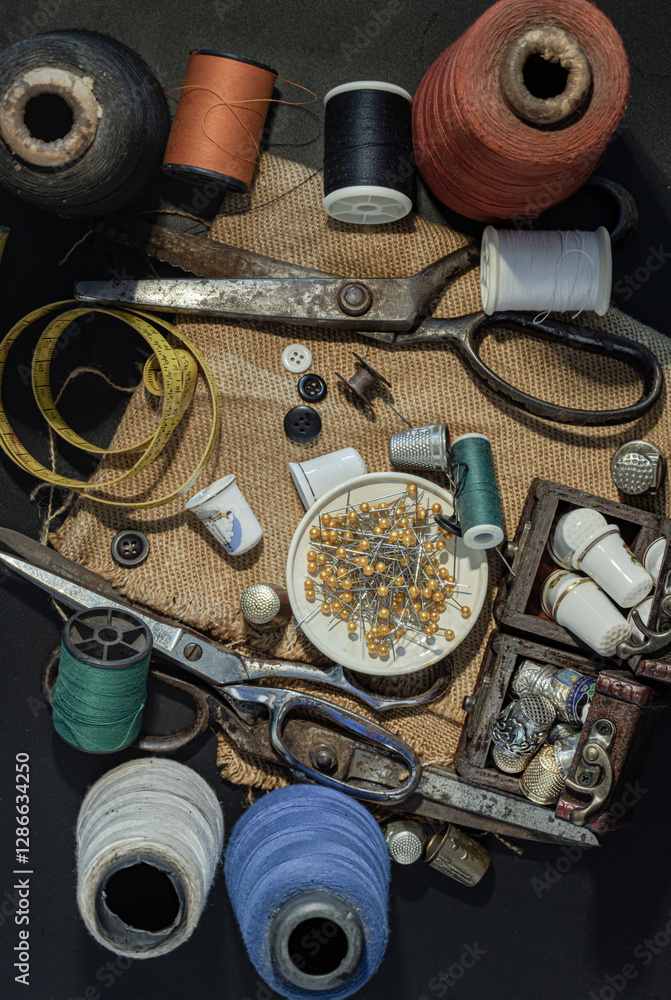 Steel scissors, Spools of thread of various colors, Thimbles in small wooden treasure chest, Sewing needles stuck in a green miniature spools thread and Measuring tape including pins in small tray.