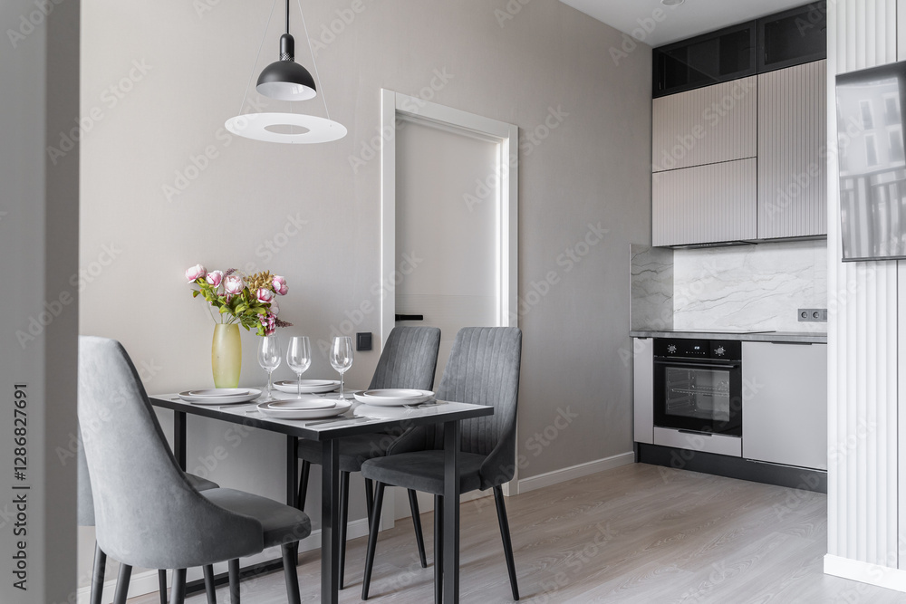 Fototapeta premium design of modern apartment in calm shades of gray and beige. Kitchen interior. plates, glasses, and vase of pink flowers on kitchen table. table and grey chairs in kitchen. Modern flat. inside home