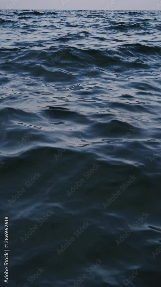 A serene video capturing gentle waves on a dark, moody sea. The low-angle shot emphasizes the texture and movement of the water's surface. Mobile wallpaper ratio. A serene video capturing gentle waves on a dark, moody sea. The low-angle shot emphasizes the texture and movement of the water's surface. Mobile wallpaper ratio.