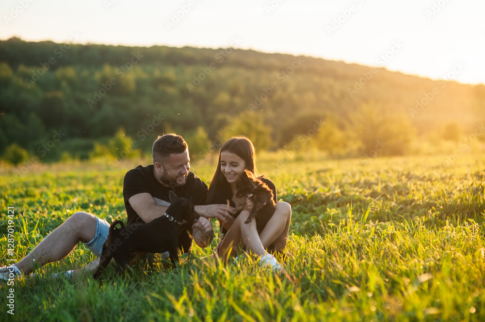Portrait of a Energetic Black pinscher dog, playing with a Happy couple with puppy, Running on a Lawn in a beautiful forest. Cheerful People Petting and Playing with a Dog. Portrait of a Energetic Black pinscher dog, playing with a Happy couple with puppy, Running on a Lawn in a beautiful forest. Cheerful People Petting and Playing with a Dog.
