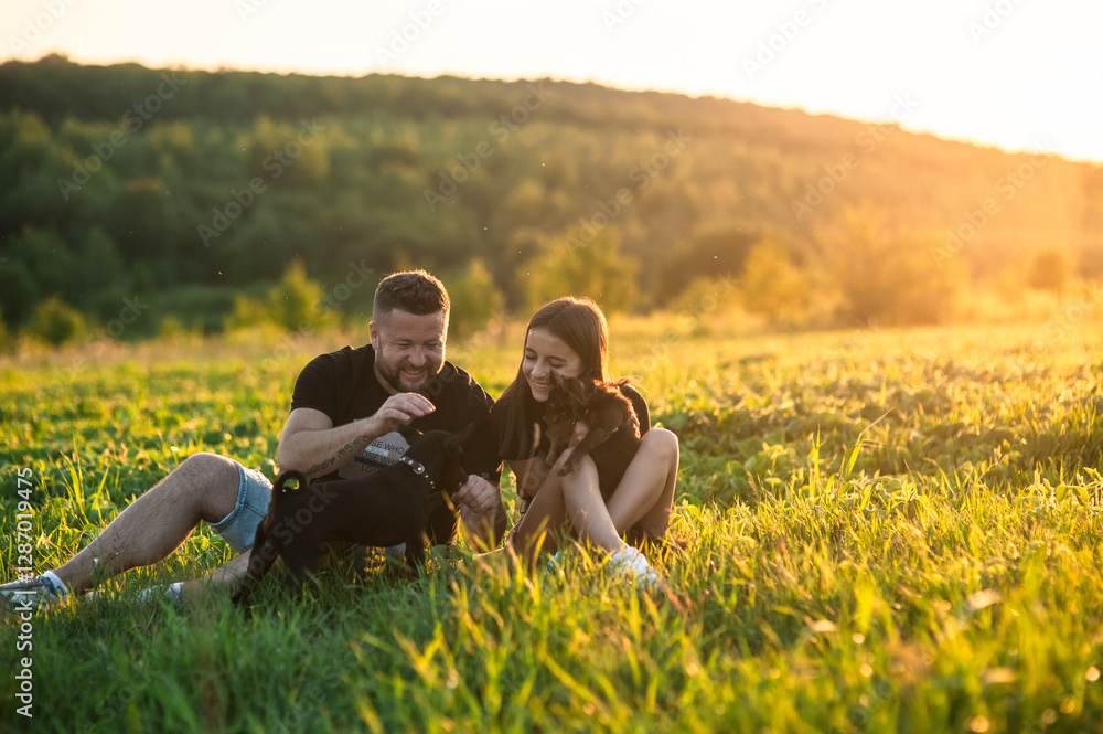 Portrait of a Energetic Black pinscher dog, playing with a Happy couple with puppy, Running on a Lawn in a beautiful forest. Cheerful People Petting and Playing with a Dog. Portrait of a Energetic Black pinscher dog, playing with a Happy couple with puppy, Running on a Lawn in a beautiful forest. Cheerful People Petting and Playing with a Dog.
