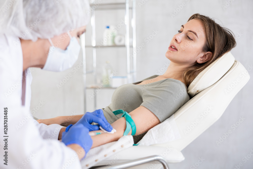 Fototapeta premium Young long-haired girl lying at white examination couch before intravenously injection at treatment room