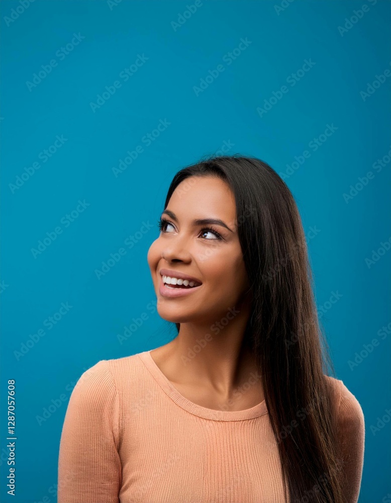 Fototapeta premium Close-up portrait of a cheerful young woman with long hair, looking curiously at copy space on a vibrant blue background. 