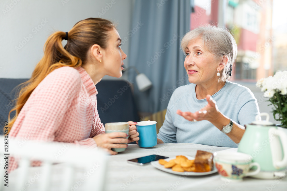 Caucasian young woman and her mature mother sitting at table, talking and drinking tea. Caucasian young woman and her mature mother sitting at table, talking and drinking tea.