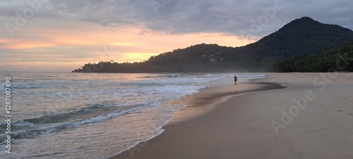 Um turista passeando durante o pôr-do-sol em um dia nublado com muitas cores no céu, na praia do Félix, em Ubatuba, litoral norte paulista, Brasil.
