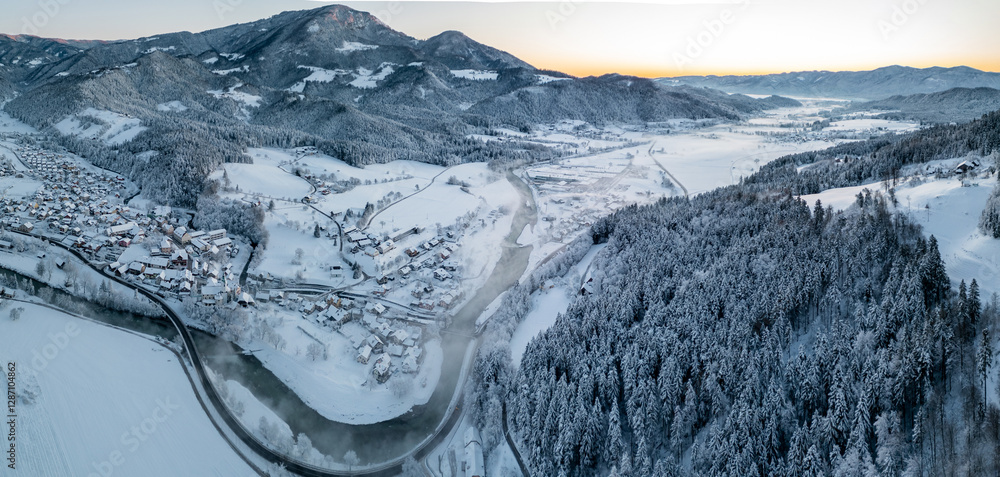 Beautiful panorama of village of Ljubno ob Savinji in cold winter morning. Visible haze from the river, sun rising up and smoke coming out of smokestacks.
