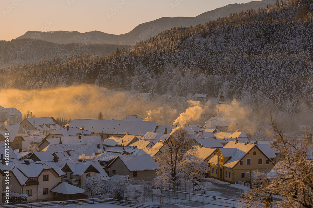 Beautiful village of Ljubno ob Savinji in cold winter morning. Visible haze from the river, sun rising up and smoke coming out of smokestacks.