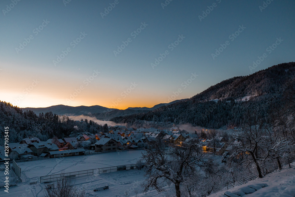 Beautiful village of Ljubno ob Savinji in cold winter morning. Visible haze from the river, sun rising up and smoke coming out of smokestacks