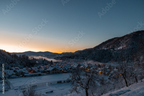 Obraz na płótnie Beautiful village of Ljubno ob Savinji in cold winter morning. Visible haze from the river, sun rising up and smoke coming out of smokestacks w salonie