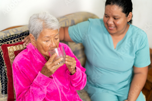 Nurse assisting elderly woman drinking water on sofa photo