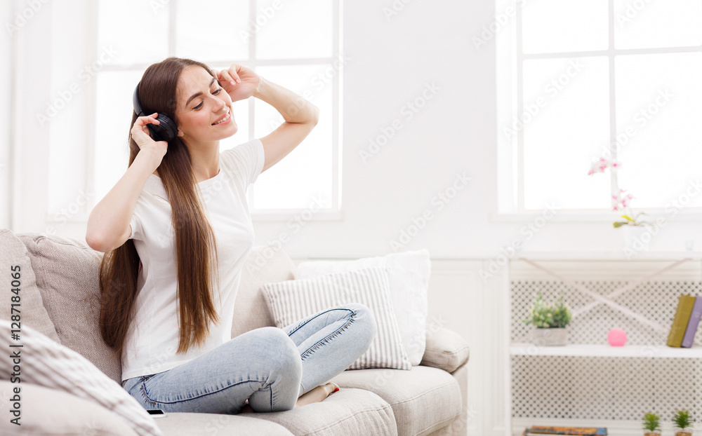 Happy girl in headphones at home. Sitting comfortably on beige sofa listening to music while. Copy space Happy girl in headphones at home. Sitting comfortably on beige sofa listening to music while. Copy space