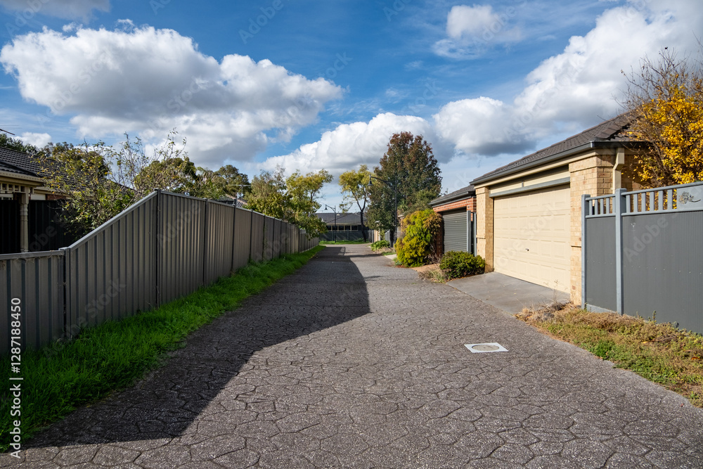 A paved and shared driveway lined with garages of residential suburban houses and boundary fence in a neighborhood of Australia. A paved and shared driveway lined with garages of residential suburban houses and boundary fence in a neighborhood of Australia.