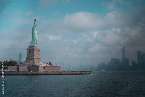 Distant view of the Statue of Liberty on Liberty Island, New York City, with a cloudy sky.