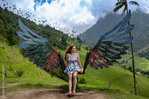 woman in cocora valley in a colorful dress sits on a decorative winged swing in the green Cocora Valley, Colombia, surrounded by wax palms and dramatic mountain scenery under a partly cloudy sky.