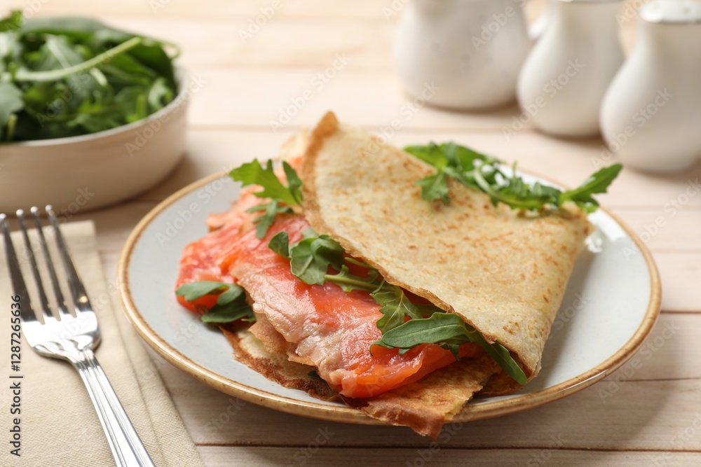 Delicious crepes with salmon and arugula on white wooden table, closeup Delicious crepes with salmon and arugula on white wooden table, closeup
