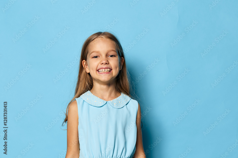 Little girl in a blue dress standing against a blue background with copy space for text or design elements Little girl in a blue dress standing against a blue background with copy space for text or design elements