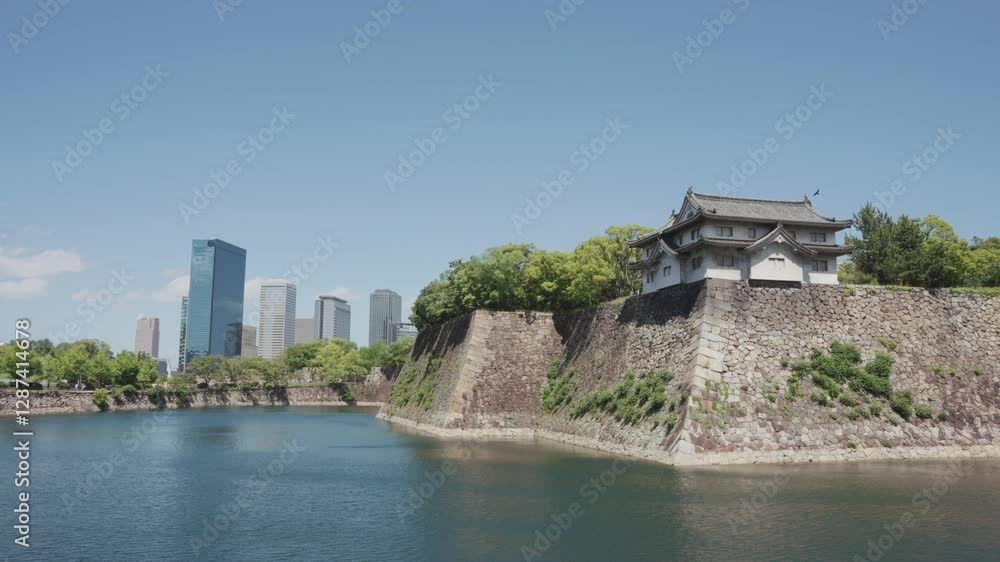 A stunning view of Osaka Castle and its moat, surrounded by lush greenery, with modern skyscrapers in the background under a bright blue sky, blending history and urban scenery. A stunning view of Osaka Castle and its moat, surrounded by lush greenery, with modern skyscrapers in the background under a bright blue sky, blending history and urban scenery.