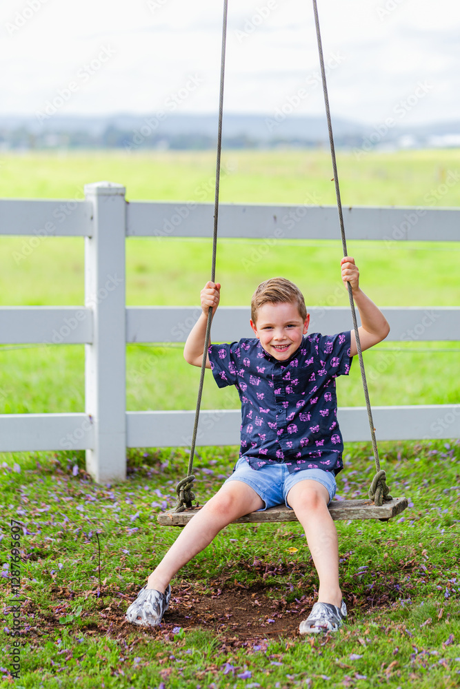 Smiling young boy alone on swing in country Smiling young boy alone on swing in country