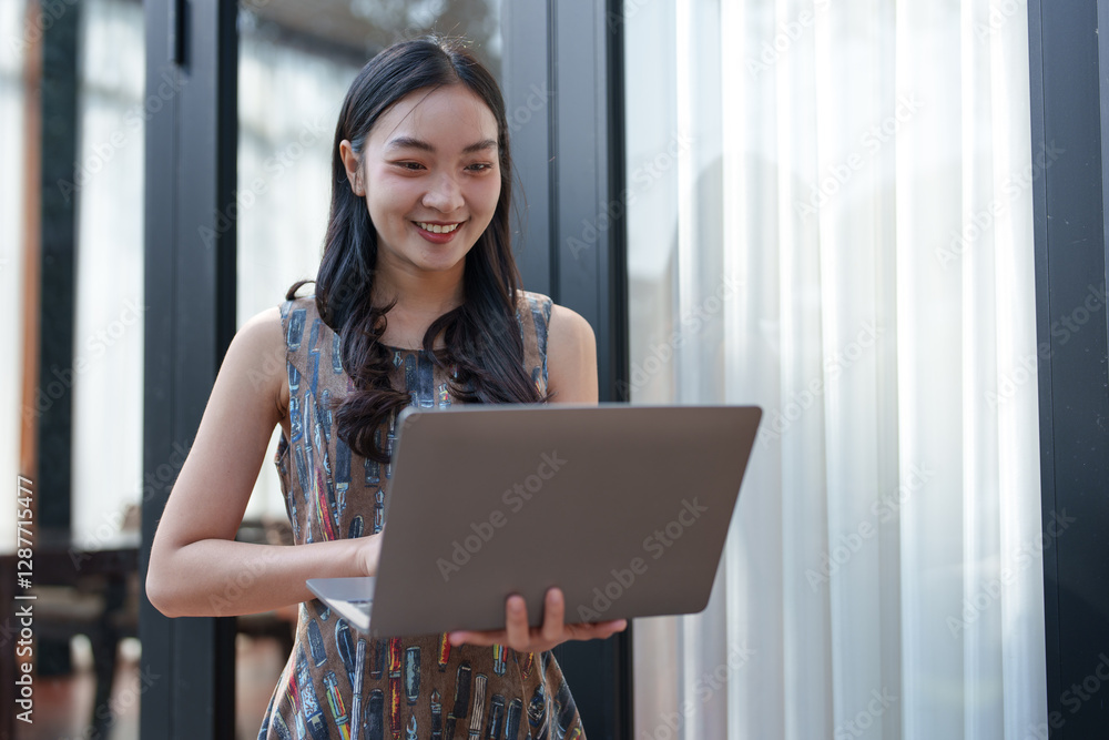 Young asian freelancer smiling while using her laptop, working remotely from a modern co-working space, enjoying the flexibility and increased productivity of remote work Young asian freelancer smiling while using her laptop, working remotely from a modern co-working space, enjoying the flexibility and increased productivity of remote work