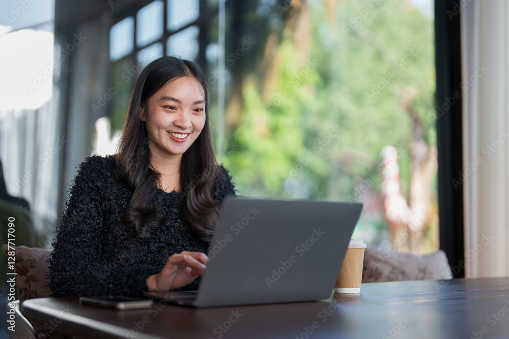 Young asian freelancer smiling and working on her laptop in a cafe, enjoying a productive workday in a relaxed atmosphere with a takeaway coffee Young asian freelancer smiling and working on her laptop in a cafe, enjoying a productive workday in a relaxed atmosphere with a takeaway coffee