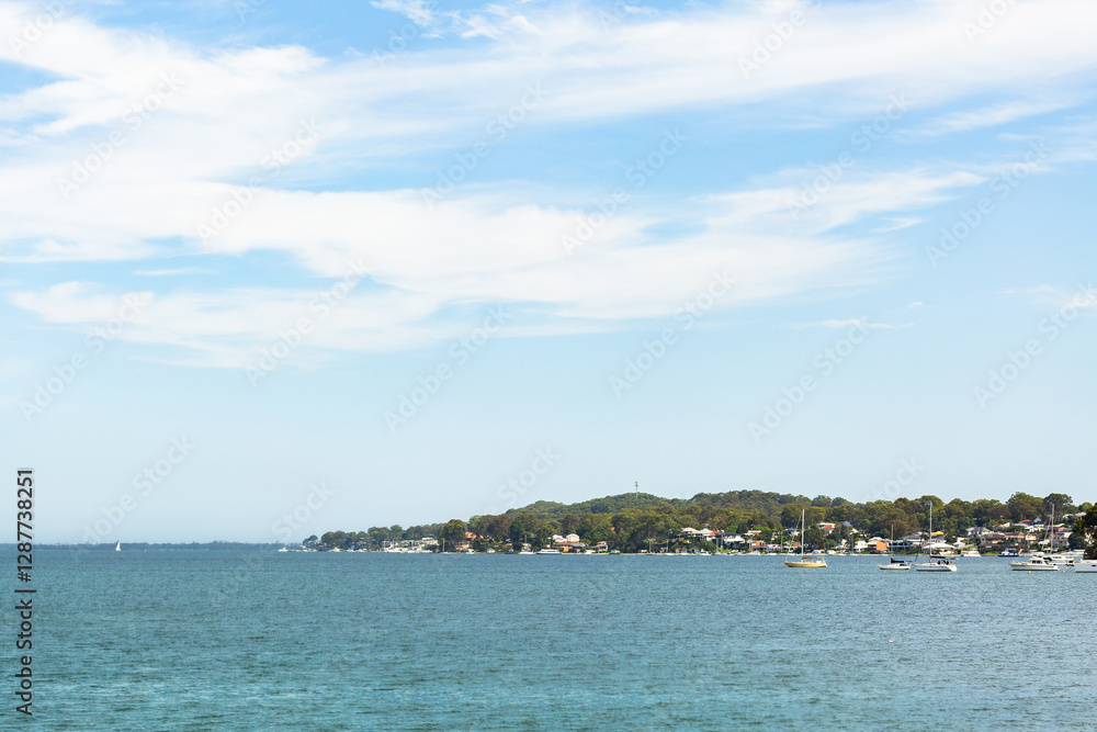 Coastal scenery with headland out in water with boats under blue sky with thin clouds Coastal scenery with headland out in water with boats under blue sky with thin clouds