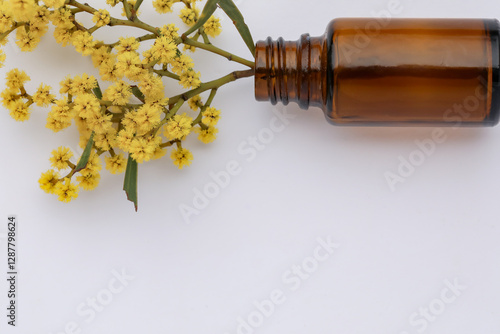 Basic white background image featuring small isolated amber glass vial with yellow wattle flowers