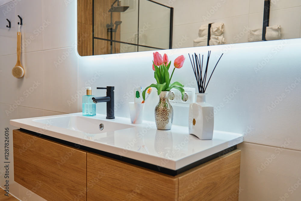 Fototapeta premium Stylish bathroom with wooden sink cabinet, black faucet and decorative elements. Contemporary interior design of bathroom with illuminated large LED mirror in modern apartment