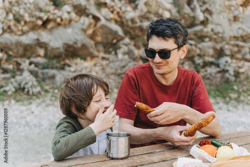 Wallpaper Mural Close-up view of father hugs his school boy son on a family picnic. Child kid and his dad taking a rest and enjoying a picnic while hiking. Boy smiles and bites the bread donut on a picnic. Torontodigital.ca