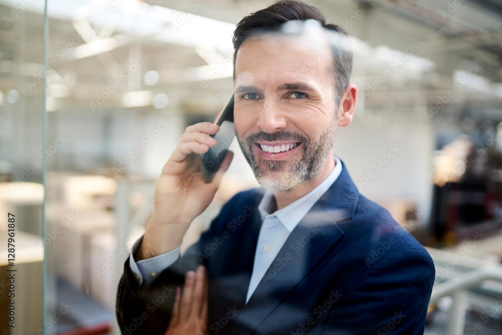 Portrait of smiling businessman on cell phone behind glass pane in a factory Portrait of smiling businessman on cell phone behind glass pane in a factory