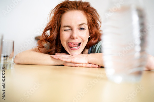 Portrait of cheerful woman winking and sticking out tongue while leaning on table at home
