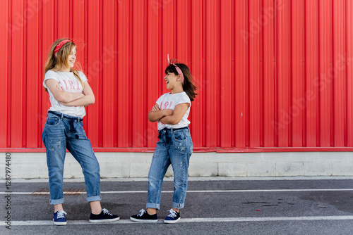 Sisters with arms crossed standing in front of a red wall photo