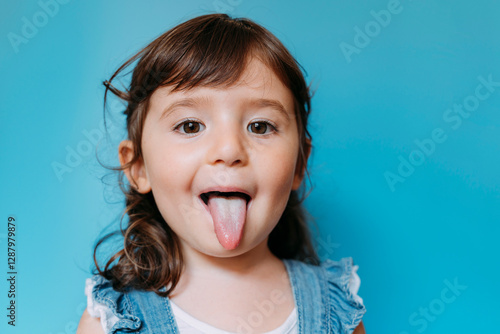 Portrait of cute little girl with tongue out on blue background