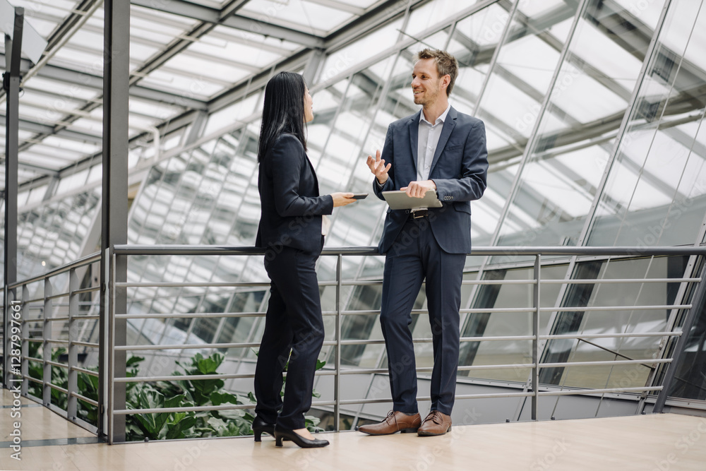 Smiling businessman and businesswoman with tablets talking in modern office building Smiling businessman and businesswoman with tablets talking in modern office building